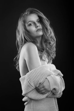 Uzun kıvırcık saçlı, şık esmer kadın gölgede poz veren çıplak omuzlu örülü bir süveter giyiyor. Tek renkli çekim.