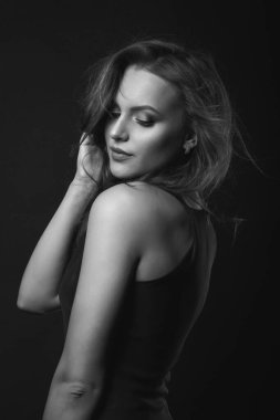 Mükemmel makyaj ve saç stili olan hassas esmer bir kadının moda stüdyosu portresi karanlık bir stüdyoda klasik siyah bir elbise giyer. Siyah ve beyaz çekim