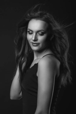 Mükemmel makyajlı ve saç stili olan muhteşem esmer bir kadının moda stüdyosu portresi karanlık bir stüdyoda klasik siyah bir elbise giyiyor. Siyah ve beyaz çekim