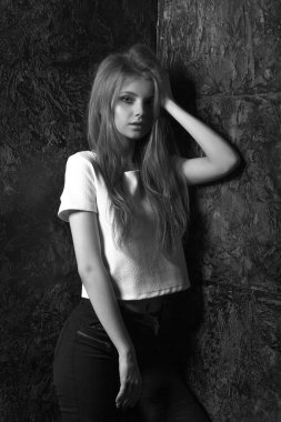 Karanlık bir odada poz veren sıradan giyinmiş şık bir kadın. Siyah ve beyaz çekim