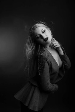 Parlak makyajlı şık bir kadının siyah beyaz stüdyo portresi çıplak bir vücutta ceket giyer.