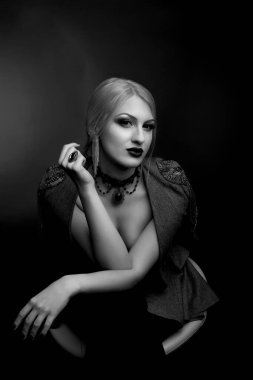 Parlak makyajlı güzel bir kadının siyah-beyaz stüdyo portresi çıplak bir vücutta ceket giyer.