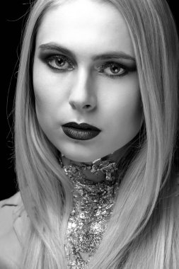 Parlak makyajlı ve boynunda folyoyla gölgede poz veren sevimli genç bir kadın. Tek renkli çekim.