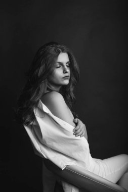 Şehvetli genç manken beyaz erkek gömleği giyer ve stüdyoda çıplak pozlar verir. Tek renkli çekim.