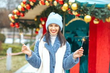 Neşeli genç kadın mavi ceket giyiyor Bengal ışıklarıyla tatilin tadını çıkarıyor