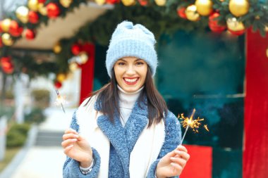 Memnun genç bayan mavi ceket giyiyor Bengal ışıklarıyla tatilin tadını çıkarıyor