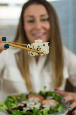 Kişi eli yemek çubuklarıyla suşi topluyor. Bulanık arka planda el yapımı suşi..