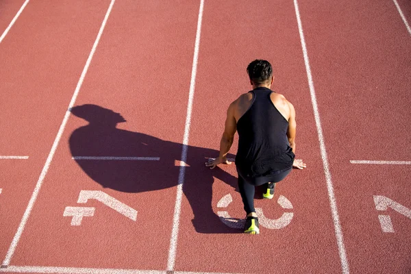 Jovem muscular homem pronto para iniciar uma pista atender . — Fotografia de Stock