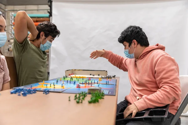 Group of youths with face masks during COVID-19 disease quarantine playing a board game.