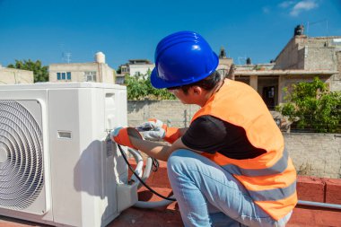 Young electrician fixing the electrical system of a air conditioning clipart