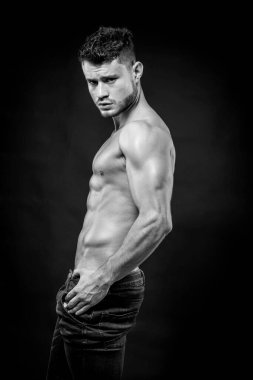Siyah arka planda kot şortlu, kaslı, üstsüz genç bir adam. Siyah ve beyaz.