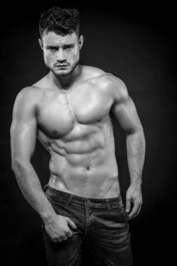 Siyah arka planda kot şortlu, kaslı, üstsüz genç bir adam. Siyah ve beyaz.