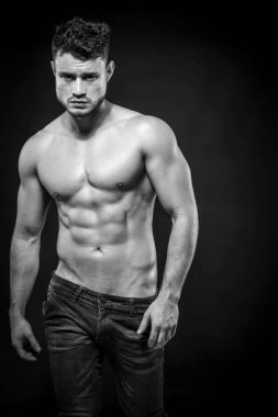 Young muscular shirtless man with denim shorts on dark background. Black and white. clipart