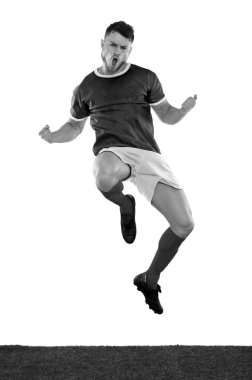 Yeşil tişörtlü genç futbolcu beyaz arka planda duygularla zıplıyor ve çığlık atıyor. Siyah ve beyaz.