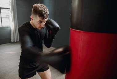 Genç bir sporcu boks çantasına vuruyor. Boksör ringde yumruk pratiği yapıyor. Sporcu kum torbasıyla saldırır..