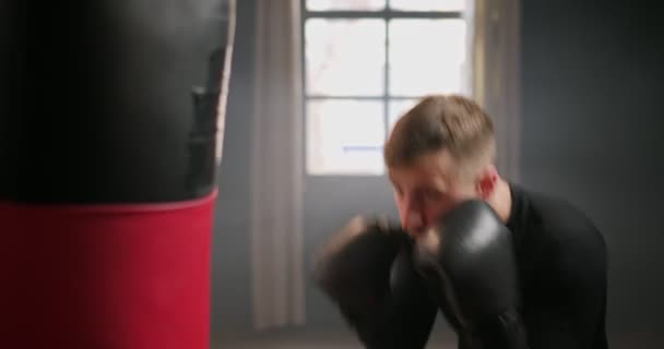 Boxning, atletisk man fighter tränar sina slag, slår en slagsäck, träningsdag i boxning gym, slår med fötterna, bakgrundsbelysning. — Stockvideo