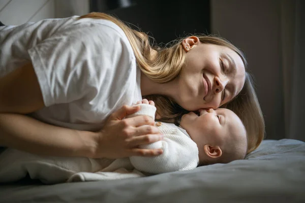 Happy woman looks at her baby and smiles. Beautiful baby smiles at mother. Mother with her own baby. Stock Photo