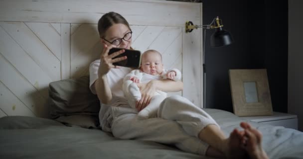 赤ん坊を持つ若い女性は自画自賛する。赤ん坊を持った若い母親がビデオ通話をする。現代の若い母親。子供を持つ現代女性. — ストック動画