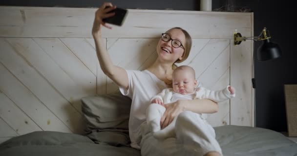 Fiatal nő babával szelfit készít. Egy kismamának van egy videohívása. Modern fiatal anya. Modern nő egy gyerekkel. — Stock videók