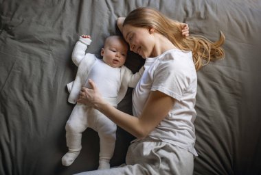Bebek annesinin üzerine yatar ve güler. Genç ve güzel bir kadın küçük kızına bakıyor. Küçük kız annesinin kollarında gülüyor..