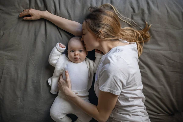 Mom with her baby lies and looks at the camera from the top. Beautiful young woman with her baby. Mother and daughter. Happy family. Stock Picture