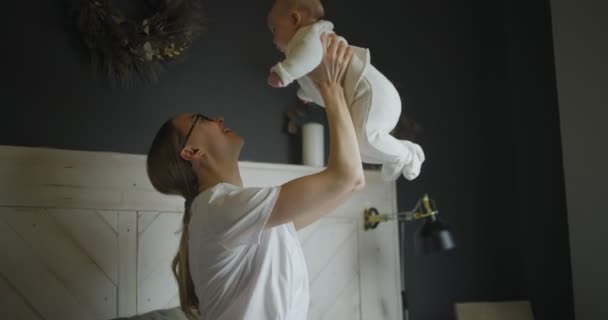 Gelukkige jonge vrouw tilt haar baby op. Jonge moeder met haar baby. Baby meisje lachen in haar moeders armen. — Stockvideo