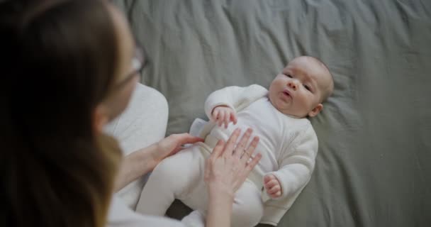 Mooie moeder met haar baby. Jonge mooie vrouw kijkt naar haar dochtertje. Baby meisje lachen in haar moeders armen. — Stockvideo