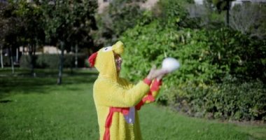 Tavuk gibi giyinmiş bir kız yumurtanın tepesine yumurta atar ve onu geri yakalar. Tavuk kostümü giymiş bir kadının komik videosu. Yumurtalı tavuk. Kız ve tavuk yumurtası..