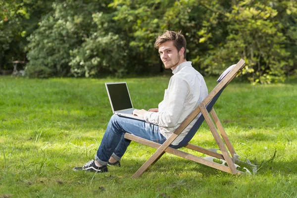 Homem no perfil sentado com computador portátil na cadeira de jardim Imagem De Stock