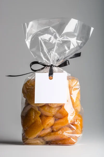 Plastic bag of dried apricots with ribbon and blank label — Stock Photo, Image