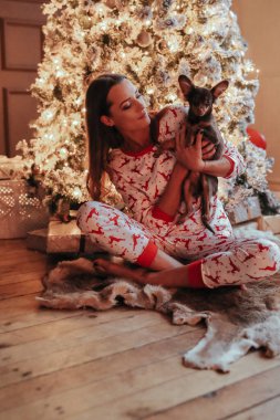 Noel etkinliği sırasında Noel ağacının yanında poz veren güzel pijamalı genç bir kadın.