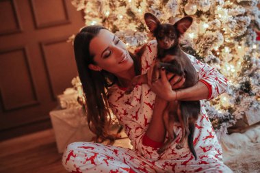 Noel etkinliği sırasında Noel ağacının yanında poz veren güzel pijamalı genç bir kadın.
