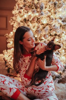 Noel etkinliği sırasında Noel ağacının yanında poz veren güzel pijamalı genç bir kadın.