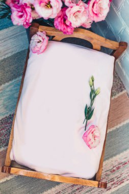 Üzerinde pembe güller ve tahta arka planda beyaz şakayıklar olan düğün davetiyesi.