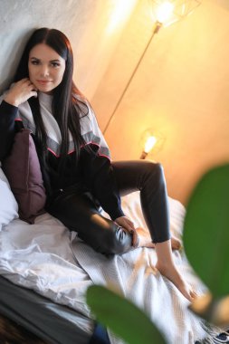 Deri pantolonlu güzel kız, bir yatakta yatıyor.