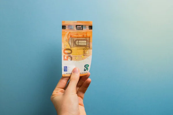 Mavi arka planda 50 Euro 'luk banknot tutuyor. Para, finans, zenginlik, iş konsepti.