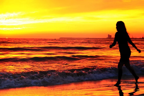 silueta de mujer, en la puesta del sol a lo largo de la costa del océano
