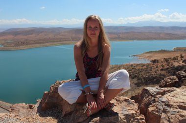 Genç bir kadın kayanın üzerinde oturup kameraya bakmak.