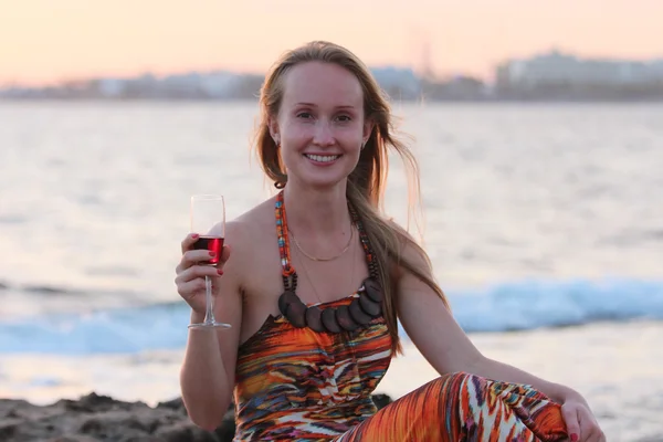 Une belle femme assise sur la plage et buvant du vin . — Photo