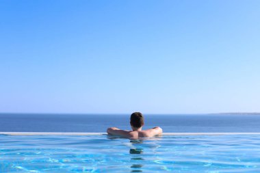 Denize bakan mavi bir havuzun kenarında dinlenen genç bir adamın arka görüntüsü. yaz tatili konsepti