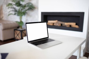 Beyaz bir masada, şömine ve yeşilliğin arka planında boş bir ekran ve metin için arka plan olan bir bilgisayar. İçerik eklemek için şablonu düzenle.