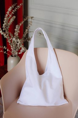 Beyaz pamuk alışveriş torbası iç taraftaki bej bir sandalyenin üzerinde duruyor. dizaynınız için yer
