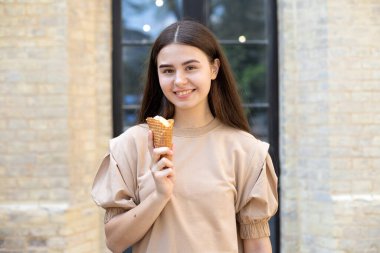 close-up of a smiling brunette girl with ice cream in a waffle cup against brick wall background clipart
