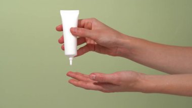 Dişi el, beyaz serum ya da krem tüpünü tutar ve onu parmağına sıkar ve yeşil izole arka planda cildine sürterek sıkar. Günlük cilt bakımı rutin koruma ve nemlendirici kavramı