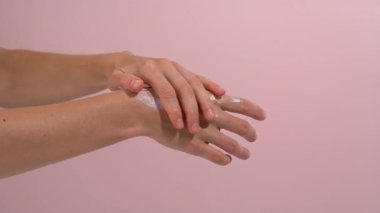 Dişi eller beyaz bir krem sürüyorlar ve pembe izole edilmiş arka planda nazikçe cilde sürüyorlar. Krem, yağ ve nemlendirici maskeler gösteren kadınlar için güzellik ritüelleri kavramı.