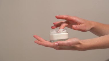 Kadın elleri şeffaf cam taklit kavanozundan kremi alır ve bej izole arkaplana sürterek cilde sürer. Besleyici kremler ve doğal özlerle parıldayan parlak cilt kavramı