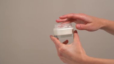 Genç bir kadının eli cam şeffaf kavanozdan krem topluyor ve arka planda bej rengi bir parmak var. Kozmetik nemlendirici krem kavramı yumuşaklık, parlaklık ve sağlıklı cilt parlaklığını geri getirir..