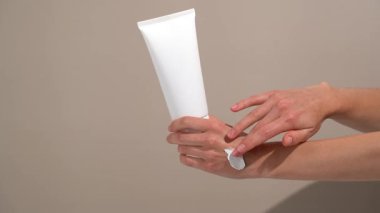 Beyaz bir krem tüpünü tutan kadın el. Bej izole arka planda dokuyu gösteren krem sürtünme. Tazelik ve canlılık kavramı bitkisel kozmetik ve hidrasyon tarafından desteklenmektedir