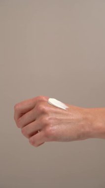 Bej rengi izole bir arka planda beyaz krem desenli kadın eli lekesi gösteren dikey bir video. Cilt kremi kavramı günlük hidrasyon, onarım ve koruyucu tedaviyi temsil eder.