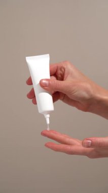 Beyaz model tüpten serumu kadının parmağına uyguladığı ve bej arka planda deriye sürttüğü dikey video. Nemlilik, esneklik ve canlanma için cilt serumu kavramı